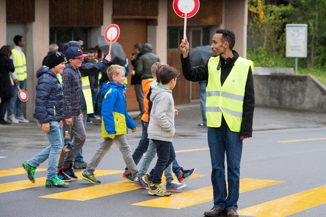 Ein Asylbewerber stoppt den Verkehr vor einem Fussgängerstreifen, den Schulkinder zum Überqueren der Strasse benützen.